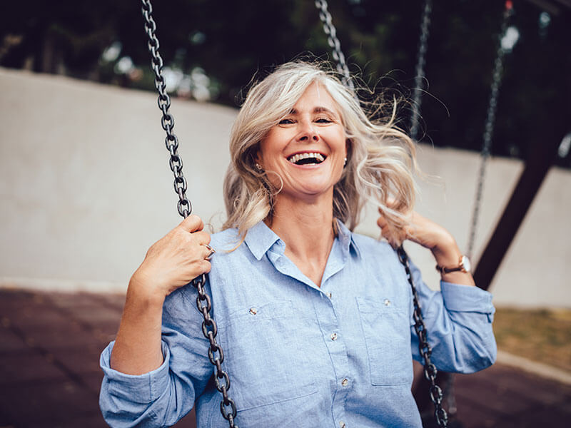 mature woman laughing outdoors on swing